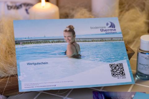Gutschein der Bodensee-Therme Konstanz neben einem Duschgel, vor einer Kerze und einem Schwamm